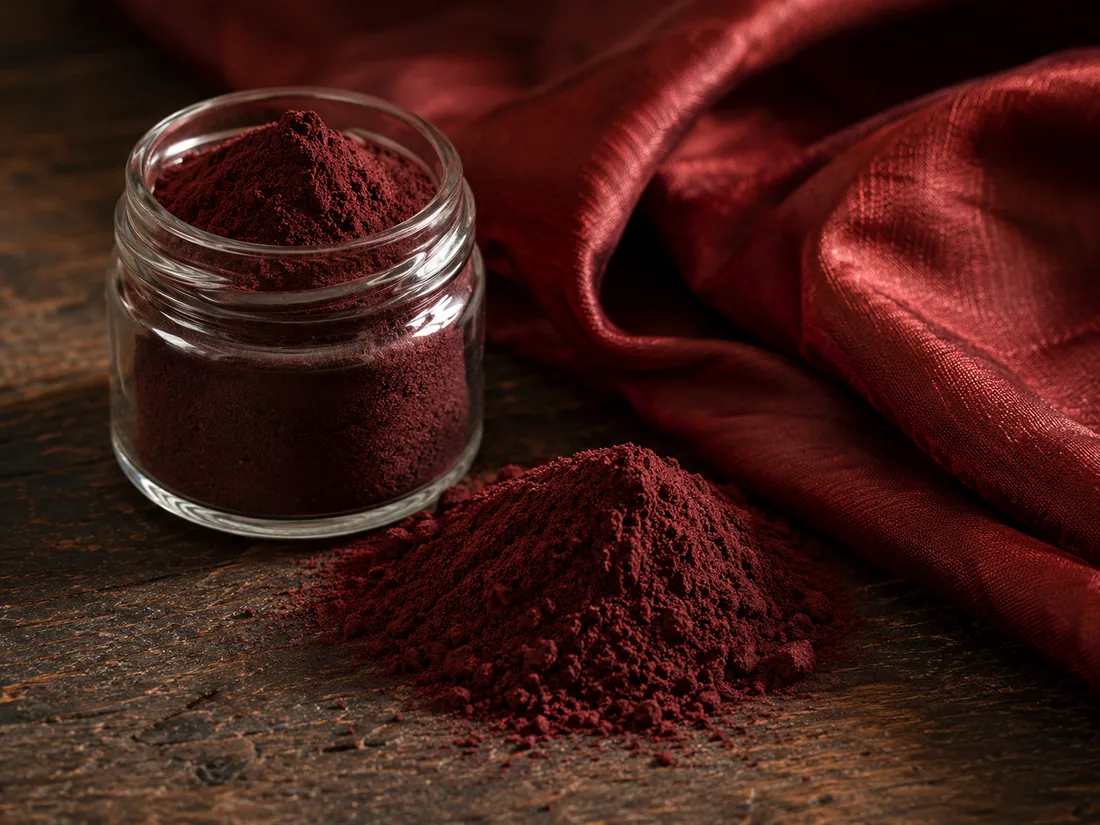 Dark red lac dye powder in a glass jar with crimson naturally-dyed silk